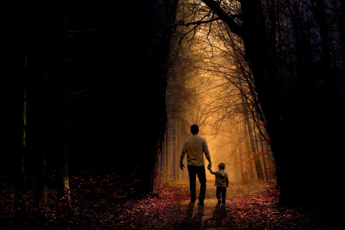 pere-fils-foret-magique-chemin-spirituel-reve Père et fils marchant main dans la main sur un chemin forestier éclairé symbolisant le lien profond et la guidance parentale