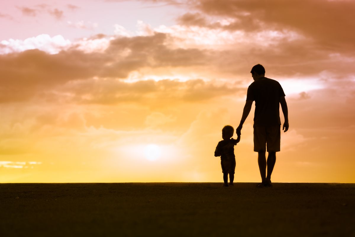 pere-fils-silhouette-coucher-soleil-avenir-protection Silhouettes d'un père tenant la main de son fils au coucher du soleil illustrant l'amour parental et le cheminement