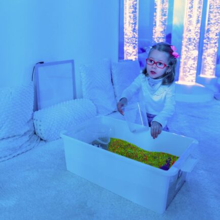 Petite fille en séance Snoezelen explorant du matériel sensoriel dans un espace multisensoriel adapté aux enfants avec éclairage thérapeutique
