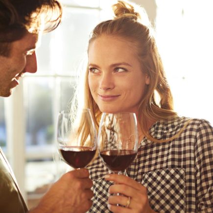 Une femme et un homme échangent des regards complices sur fond de verres de vin, un jeu de séduction silencieux